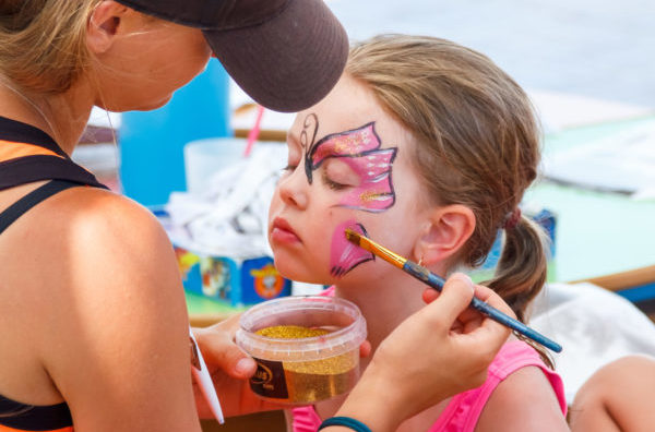 A little girl draws a pink butterfly on her face with aquagrim. Entertainment for children on vacation at the sea